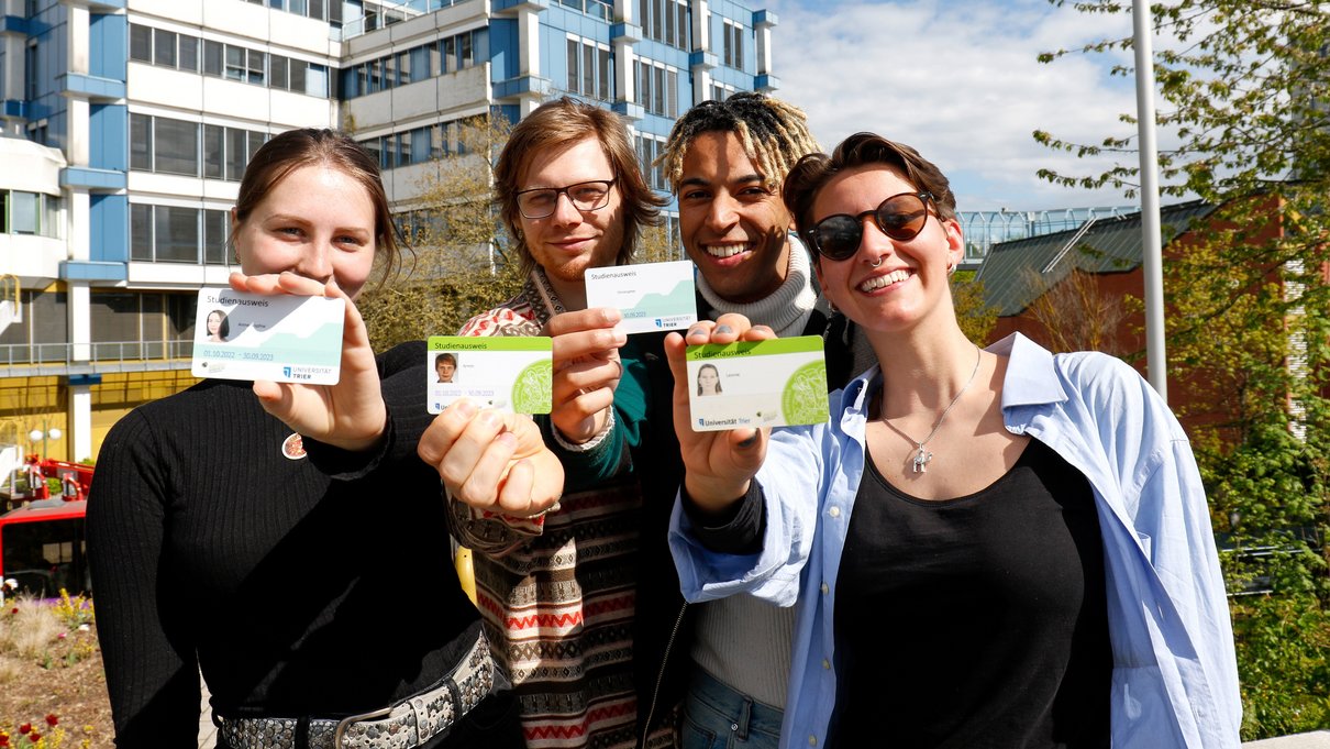 Studierende halten vor dem Gebäude AB ihren Studienausweis (TUNIKA) in die Kamera. 