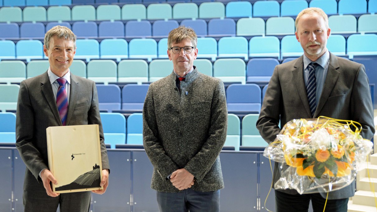 Mit Universitätswein bedankte sich Präsident Prof. Dr. Michael Jäckel (Mitte) bei Prof. Dr. Georg Müller-Fürstenberger (links), der acht Jahre lang das Vizepräsidentenamt innehatte, das in einer Feier im Audimax an Prof. Dr. Torsten Mattern übergeben wurde.