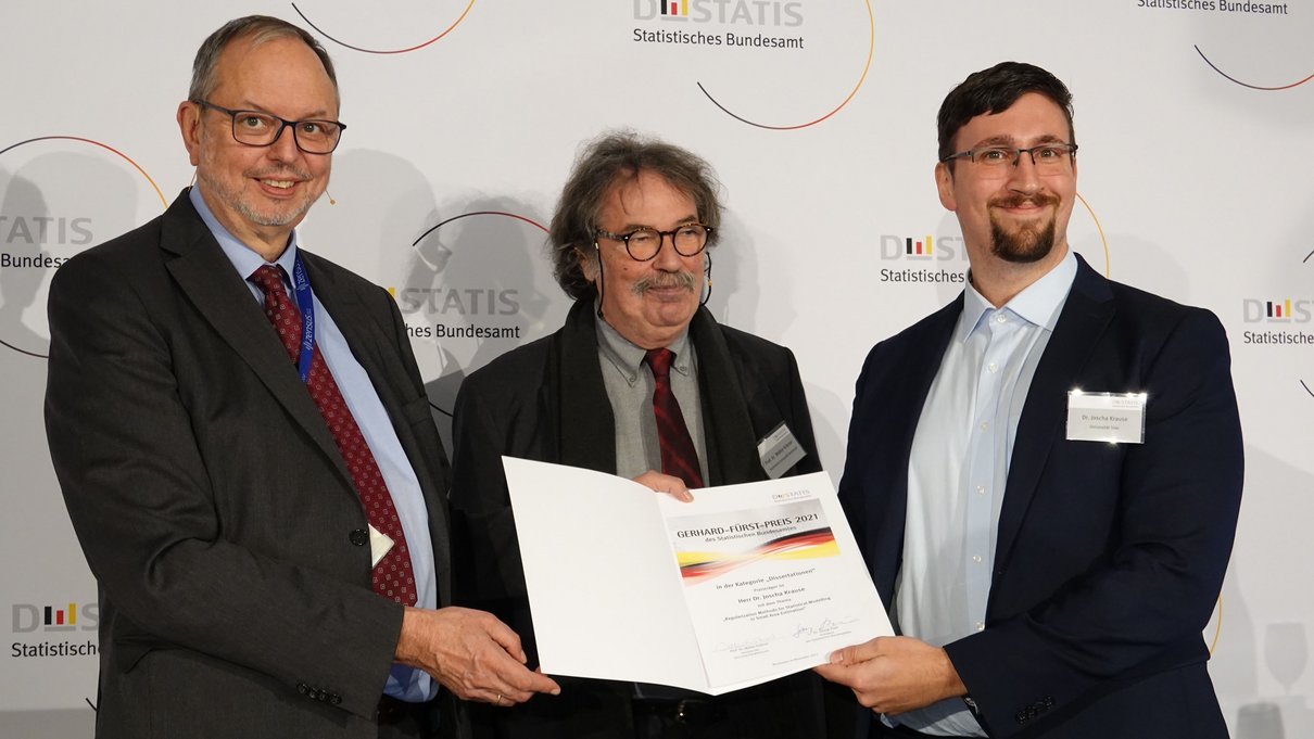 Dr. Joscha Krause (rechts) erhält den Gerhard-Fürst-Preis aus den Händen des Präsidenten des Statistischen Bundesamtes, Dr. Georg Thiel (links), und des Vorsitzenden des Gutachtergremiums, Prof. Dr. Walter Krämer. Foto: Statistisches Bundesamt (Destatis)