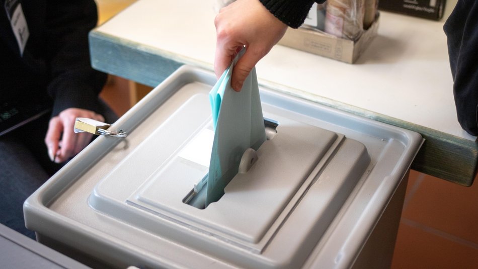 Symbolfoto mit einer Wahlbox und einem Wahlzettel der eingeworfen wird. 