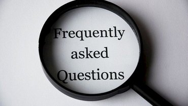 Eine Lupe liegt über den gedruckten Wörtern "Frequently asked Questions" auf einem weißen Hintergrund.