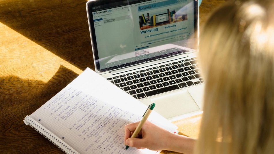 Digitale Lehre, Studentin vor dem Laptop mit Kopfhörern und Notizblock.