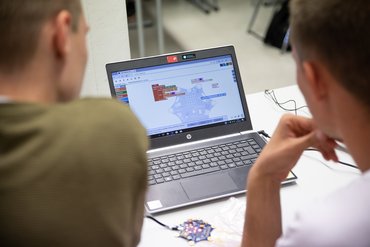 Blick über die Schulter bei zwei Personen, die an einem Laptop arbeiten.