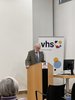 Photo of Prof. David Staines. He is an older gentleman with white hair. He is standing behind a lectern. He is wearing a brown blazer. 