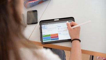 Person sitzt vor einem Tablet, auf dem die Homepage Porta zu sehen ist.