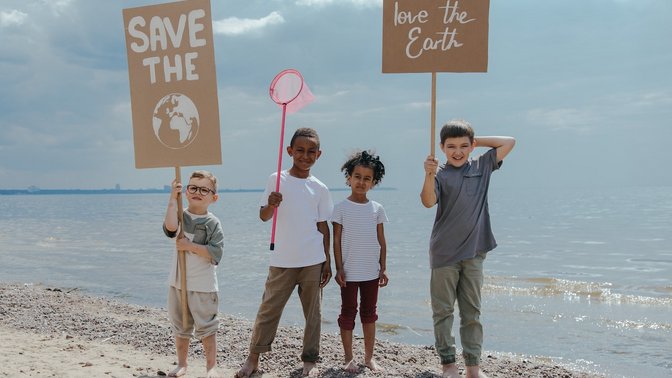 Kinder mit zwei Plakaten vor dem Meer: Safe the Earth und Love the Earth.