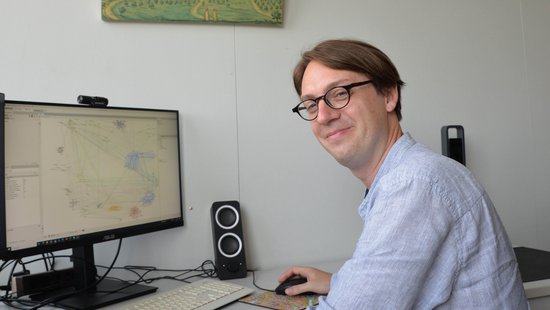 Prof. Dr. Damien Tricoire sitzt am Rechner und schaut in die Kamera