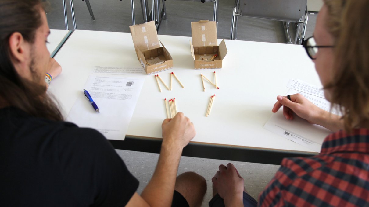 Zwei Personen mit Streichhölzern auf einem Tisch.