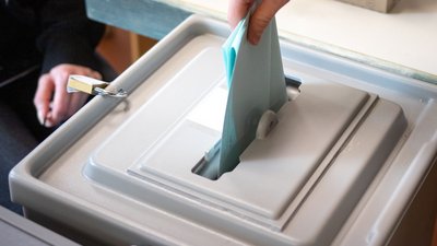 Stimmzettel wird in die Wahlurne gesteckt. 