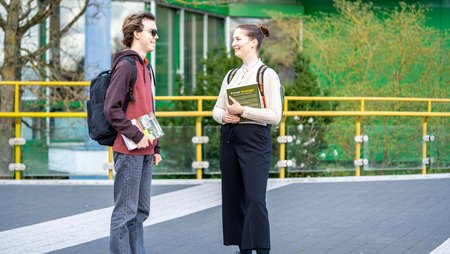 Studierende unterhalten sich auf dem Campus mit Büchern in der Hand. 