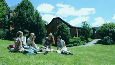 Gruppe von Studierenden sitzt auf einer Wiese am Mensa-Gebäude.