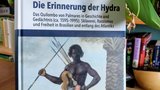 Exemplar des Buchs auf einem Tisch vor einer Zimmerpflanze; auf dem Cover ist das Bild eines afrikanischen Kriegers von Albert Eckhout abgebildet.