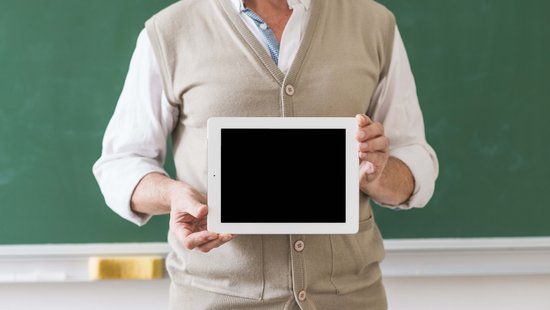 Lehrer vor einer Tafel mit Tablet in der Hand