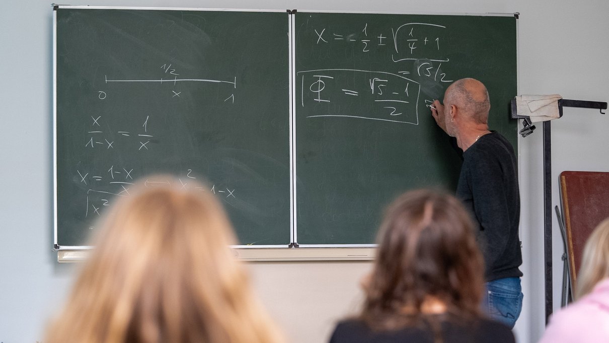 [Translate to Englisch:] Lehrer schreibt mathematische Formeln an die Tafel vor einer Schulklasse