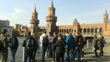 Photo shows a group of students in the field with the Oberbaumbrücke in Berlin in the background