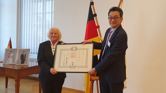 Shinichi Asazuma übergibt Hilaria Gössmann eine Urkunde in einem Rahmen