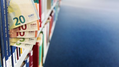 [Translate to Englisch:] Geldscheine zwischen Büchern im Regal. 