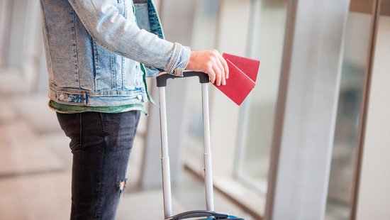 Person mit zwei Pässen in der Hand und Koffer am Flughafen Foto: Colourbox.de
