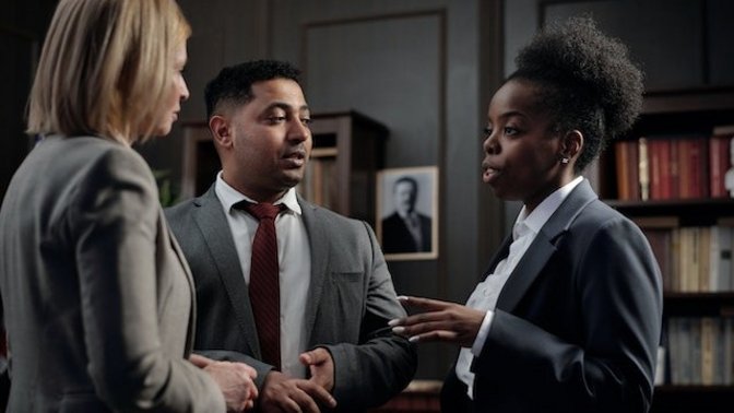 Drei Personen in formeller Kleidung im Gespräch. Eine schwarze Fraus spricht. Ein Mann und eine Frau hören ihr zu.