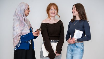 Drei Mädchen sprechen miteinander und lachen in die Kamera.