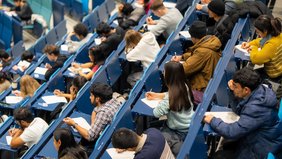 Studierende sitzen über einer Klausur im Audimax