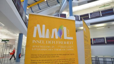 Gelbes Ausstellungsplakat Insel der Freiheit mit Bibliothek im Hintergrund