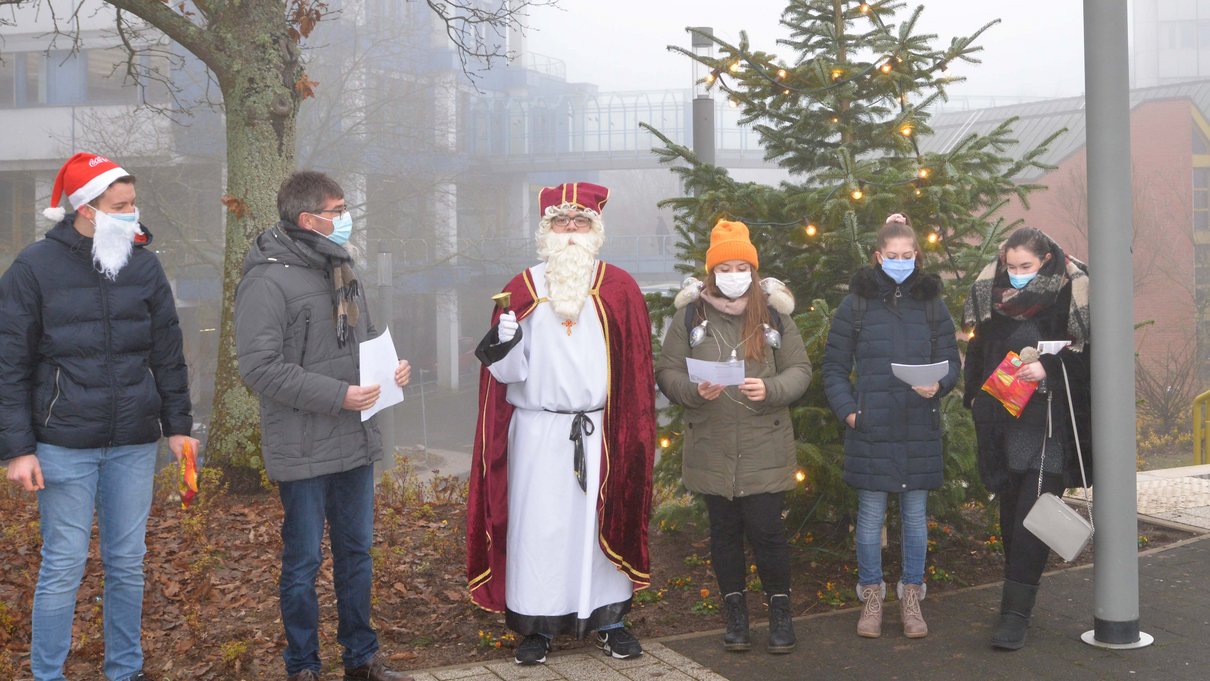 Gemeinsam sangen Universitätspräsident Prof. Dr. Michael Jäckel, der Kleeschen und seine Begleiter vor dem beleuchteten Weihnachtsbaum. 