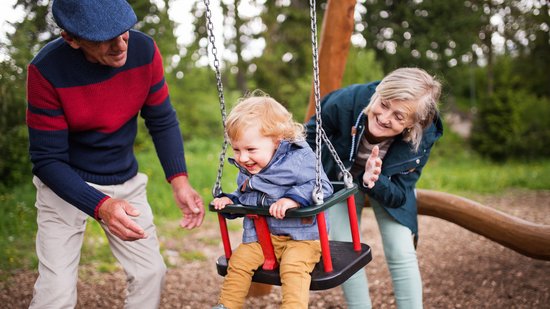 Oma und Opa sind mit einem Kind auf dem Spielplatz was schaukelt. Foto:Colourbox.de