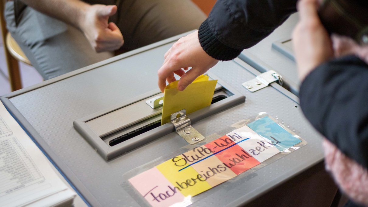Wahlurne zur StuPa-Wahl, in die jemand einen Stimmzettel wirft