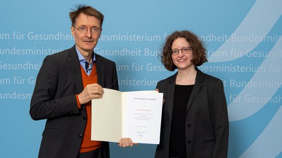 Minister Lauterbach überreicht Professorin Melanie Messer die Urkunde.
