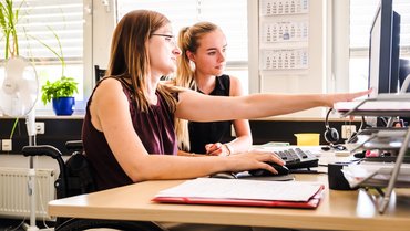 Zwei Frauen am Schreibtisch, eine im Rollstuhl