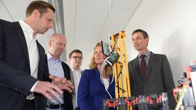 Patrick Klein, Prof. Dr. Axel Kalenborn, Lukas Malburg und Prof. Dr. Georg Müller-Fürstenberger (von links), Vizepräsident der Universität Trier, informieren Staatssekretärin Heike Raab am Beispiel eines Fischertechnik-Modells.