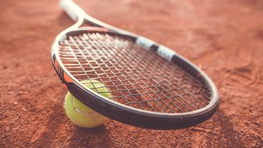 Tennisschläger, der auf einem Tennisball liegt. Hintergrund Ascheplatz.