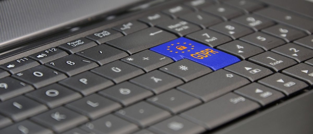 Photo of a gray computer keyboard. The Enter key is dark blue. In yellow is a lock with a circle of stars around it. Below it are the letters GDPR.
