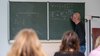 Lehrer schreibt mathematische Formeln an die Tafel vor einer Schulklasse